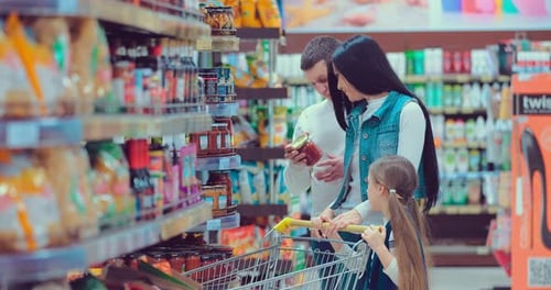 Young Famaly in Supermarket Choosing a Cans on the Rack Checking Them at First