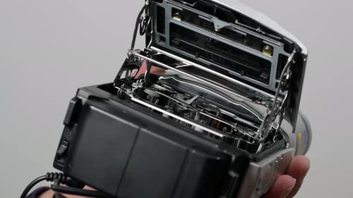 A man is changing the videotape on an old JVC camcorder. A camera from the '90s.