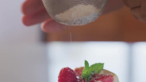 Cheesecake Garnished with Raspberry and Mint Being Dusted with Sugar