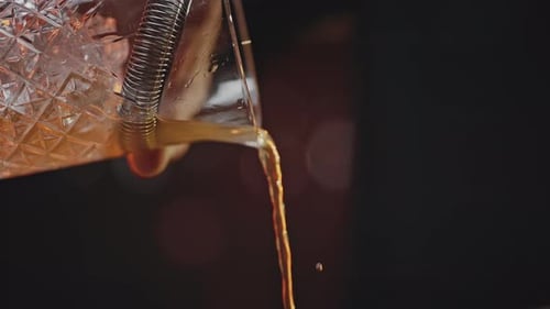 El camarero vierte el cóctel listo en un vaso con cubitos de hielo