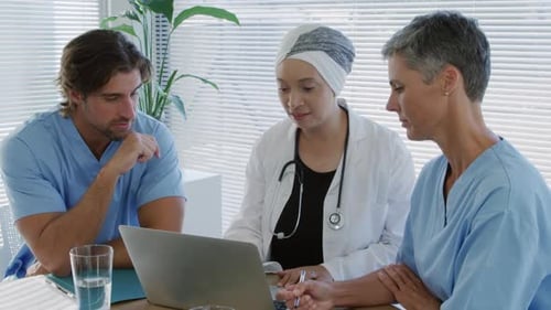 Healthcare Staff Meeting Around Laptop in Bright Office