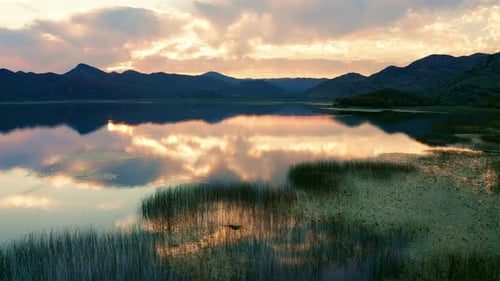 Beautiful sunset sky reflected in a lake - marsh grass and silhouettes of mountains