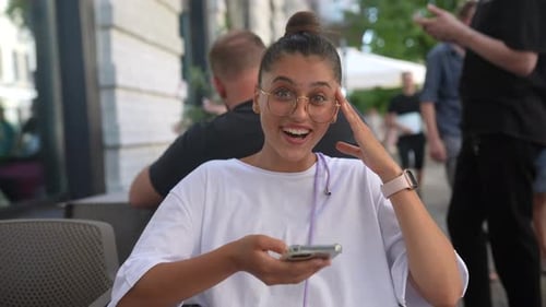 Beautiful Young Woman Sitting in Street Cafe Using a Smartphone