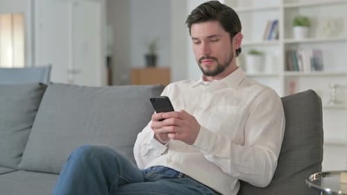 Young Adult Using Smartphone on Couch Indoors