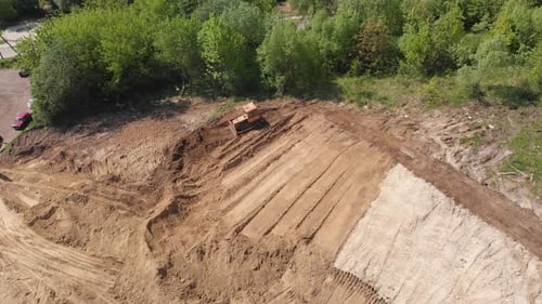 Aerial view of bulldozer flattening surface on further construction site
