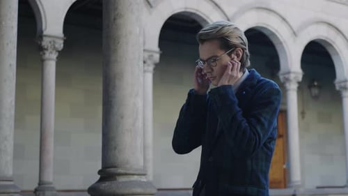 Young Man Inserts Earbuds Near Arches and Columns