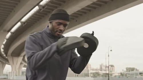 Man Shadowboxing With Mitts Under an Elevated Highway