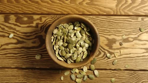 Peeled Pumpkin Seeds Fall Into A Wooden Dish On A Table