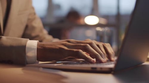 Black Businessman Texting on Laptop while Working Late in Office