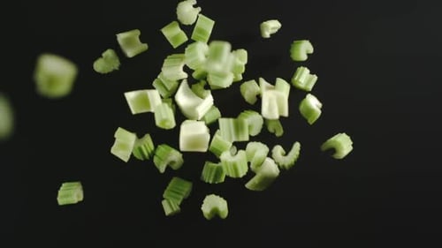 Morceaux de céleri vert frais tombant sur une surface noire