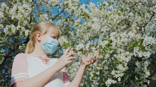 Girl in Mask Touches Spring Blossoms