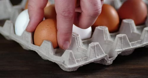 Die Männerhand nimmt rohe Eier aus einem Papierständer.