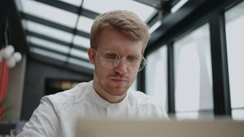 Attractive Man with Glasses is Working with Laptop in Office Modern Coworking Space for Freelancer