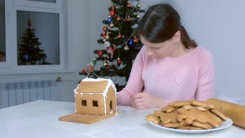 Woman Decorating a Gingerbread House at Christmas