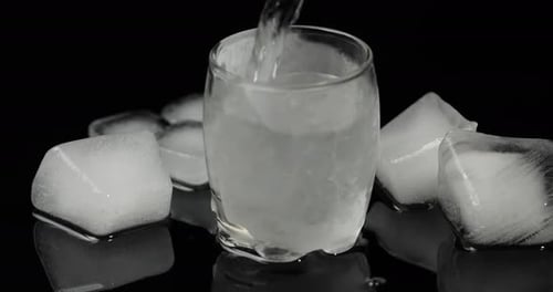Water Being Poured Into Glass Surrounded by Ice