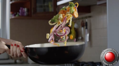Tossing vegetables in a black frying pan in kitchen