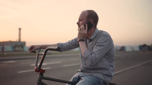 Young Man with Bmx Bicycle Uses His Phone at Sunset on the Street