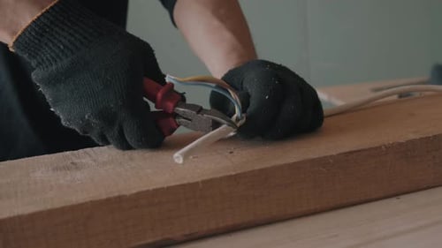 Worker Cutting Wires with Pliers on Wood Table