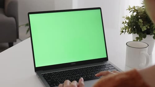 Young Asian woman using laptop computer at home with green blank monitor screen.