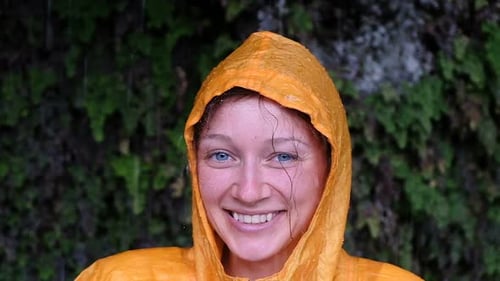 Smiling Woman in Raincoat Under Rainfall