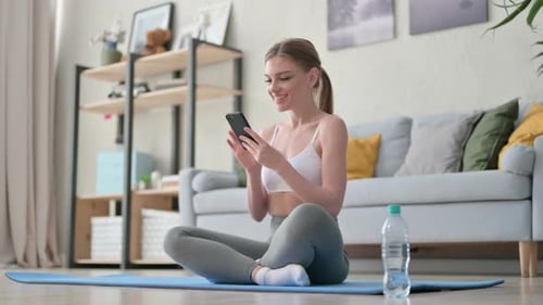 Young Woman Using Phone on Exercise Mat at Home