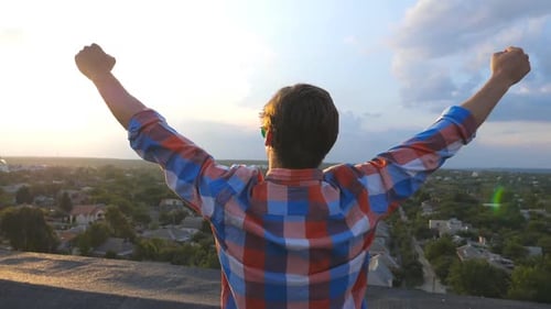 Young Adult Arms Outstretched on Rooftop at Sunset