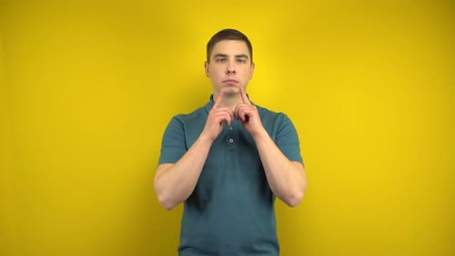 Un joven hace una sonrisa triste y alegre en su rostro con sus dedos sobre un fondo amarillo.
Hombre