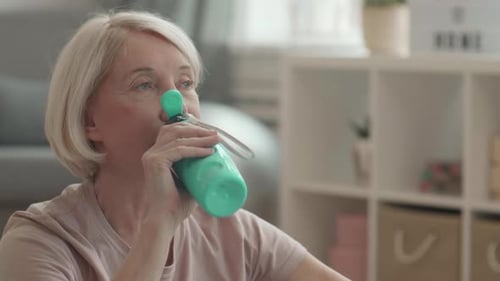 Mature Woman Drinking Water After Workout at Home