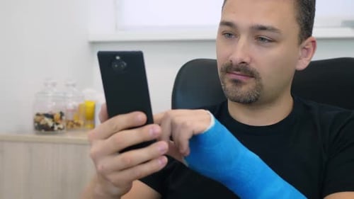 Man with Arm Cast Using Smartphone Indoors