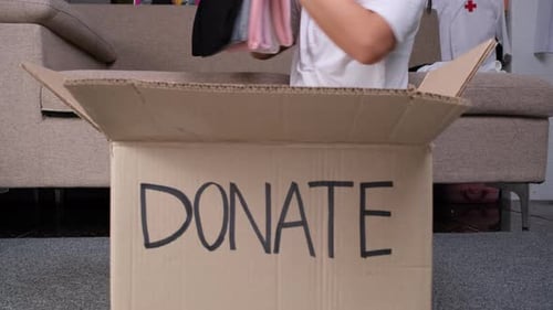 Junge Frau steckt zu Hause Kleidung in eine Spendenbox, um den Armen zu helfen. Spenden-Konzept.