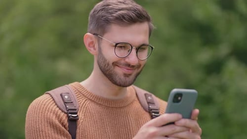Smiling Man with Glasses with a Beard Walks Through the Woods with a Backpack and Prints a Message