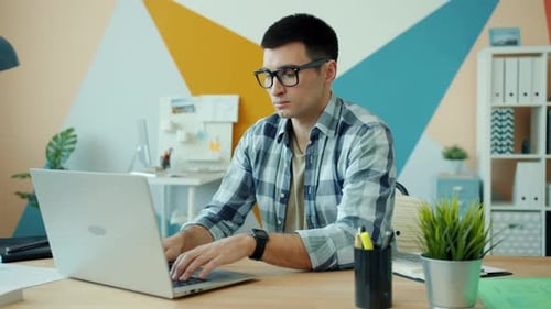 Tired Young Man Using Laptop in Office Then Touching Head Feeling Exhausted