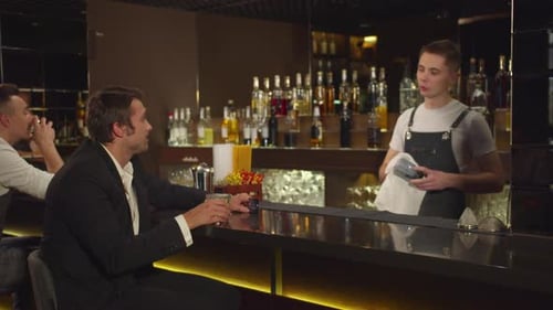 Man Sits at the Bar, Talks To Bartender and Twirls His Credit Card