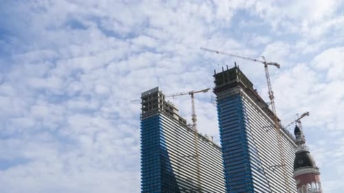 Construction of a Modern Skyscrapers Using Tower Cranes. Timelapse, Moving Clouds on Blue Sky