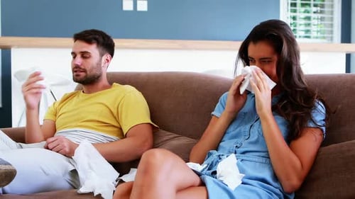 Ill Couple Sitting on Couch with Tissues