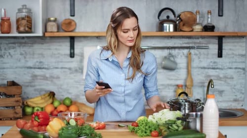 Woman Using Smartphone While Cooking Vegetables