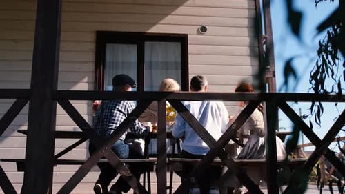 Family Members of Several Generations Sit at a Wooden Table on the Terrace Outside the House and