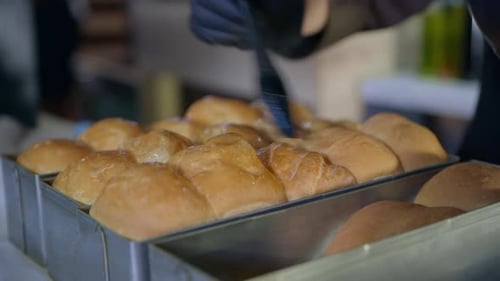 Bäckerei, Koch, Condit Woman in Handschuhen schmiert heiße duftende Brötchen, die aus dem Ofen genommen wurden, mit Silikon