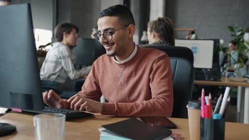 Slow Motion of Cheerful Arab Man Using Computer Typing Looking at Screen in Office