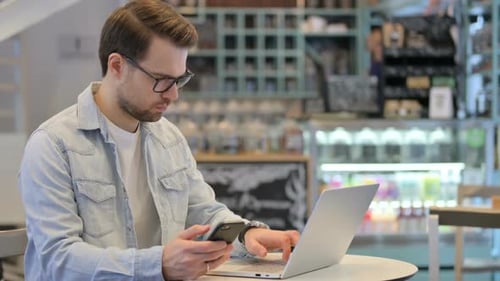 Man with Laptop Using Smartphone in Cafe