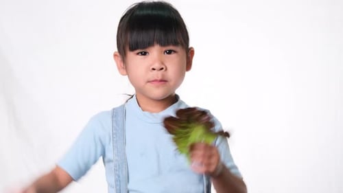Happy little girl with fresh salad with showing thumbs up on white background in studio