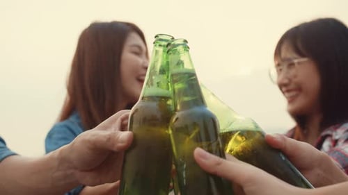 Friends Clinking Beer Bottles Together Outdoors at Sunset