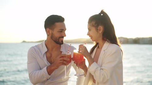 Smiling Hispanic Couple with Cocktails Kissing Against Sea