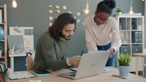 Arab Man and African American Girl Working Looking Through Documents and Using Laptop in Office