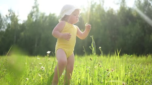 Little Funny Cute Blonde Girl Child Toddler in Yellow Bodysuit and White Hat Walking in Field with