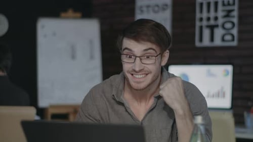 Empresario alegre mirando la pantalla del portátil y haciendo un gesto de sí en la oficina oscura