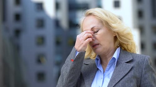 Concerned Woman in Gray Jacket Rubbing Her Eye