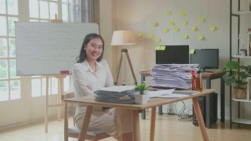 Asian Woman Crossing Arms And Smiling To Camera While Working With Documents At The Office