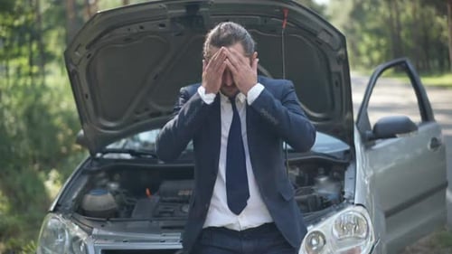 Portrait of Sad Handsome Young Man Leaning on Car Hood Holding Head in Hands Sighing