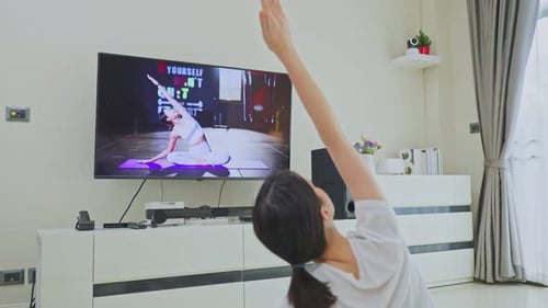 Hermosa joven asiática que se queda en casa, haciendo ejercicio, siga las instrucciones del vídeo del entrenador en línea.